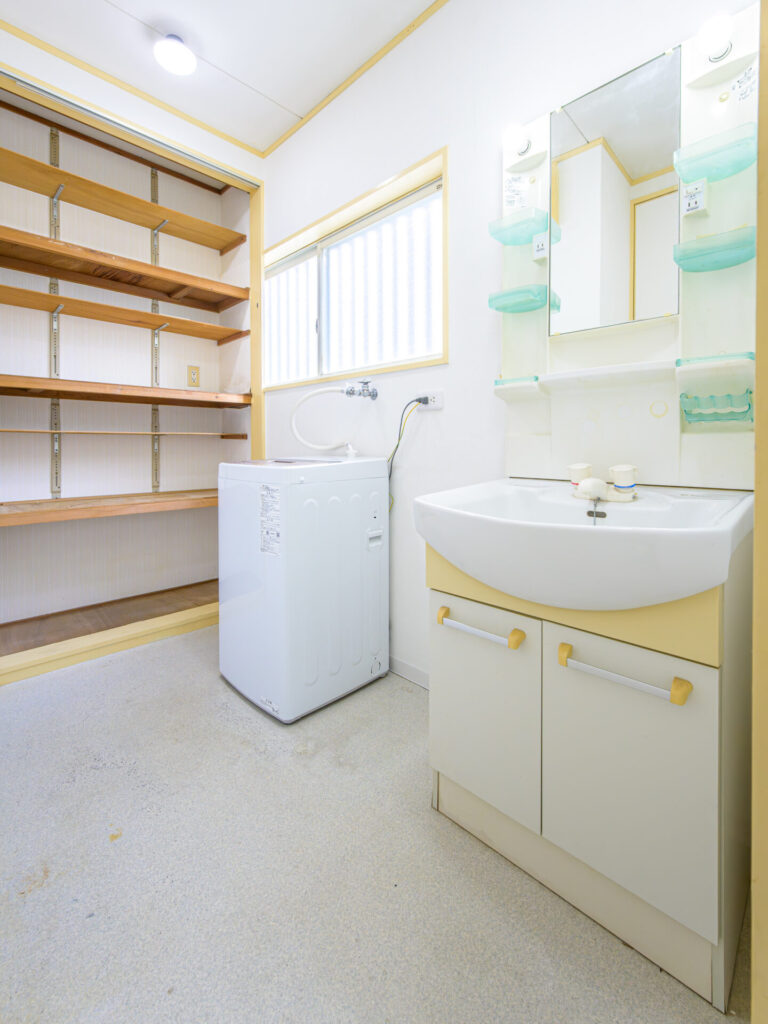 障がい者グループホームの洗面脱衣所スペース。洗濯機と独立洗面台、収納棚を完備した清潔感ある室内設備。